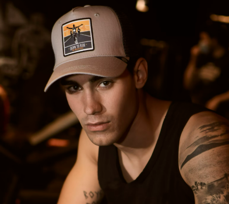 Man in a tank top and cap posing indoors.