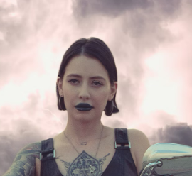 Woman with short hair and tattoos under cloudy sky.